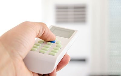 Homeowner adjusting a remote for a wall-mounted air conditioning unit